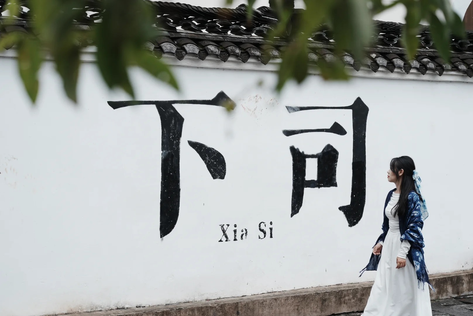 Du kh&aacute;ch chụp ảnh trước tường trắng c&oacute; chữ Hạ Tư Cổ Trấn bằng tiếng Trung 