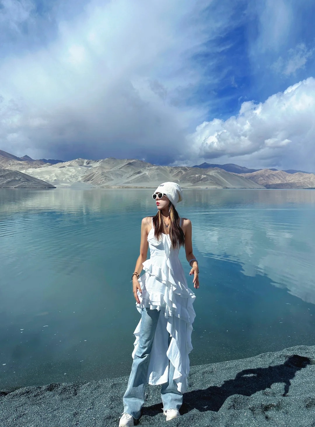 Du khách tạo dáng trước mặt hồ, phía sau là núi tuyết và trời xanh.