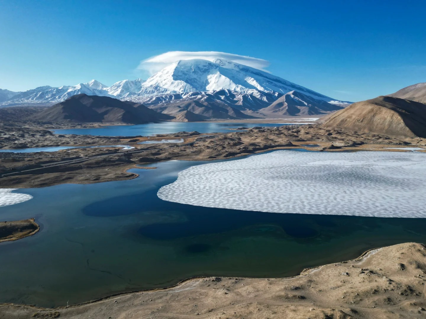 Mặt hồ phẳng lặng như gương, phản chiếu mây trắng và trời xanh cao nguyên.